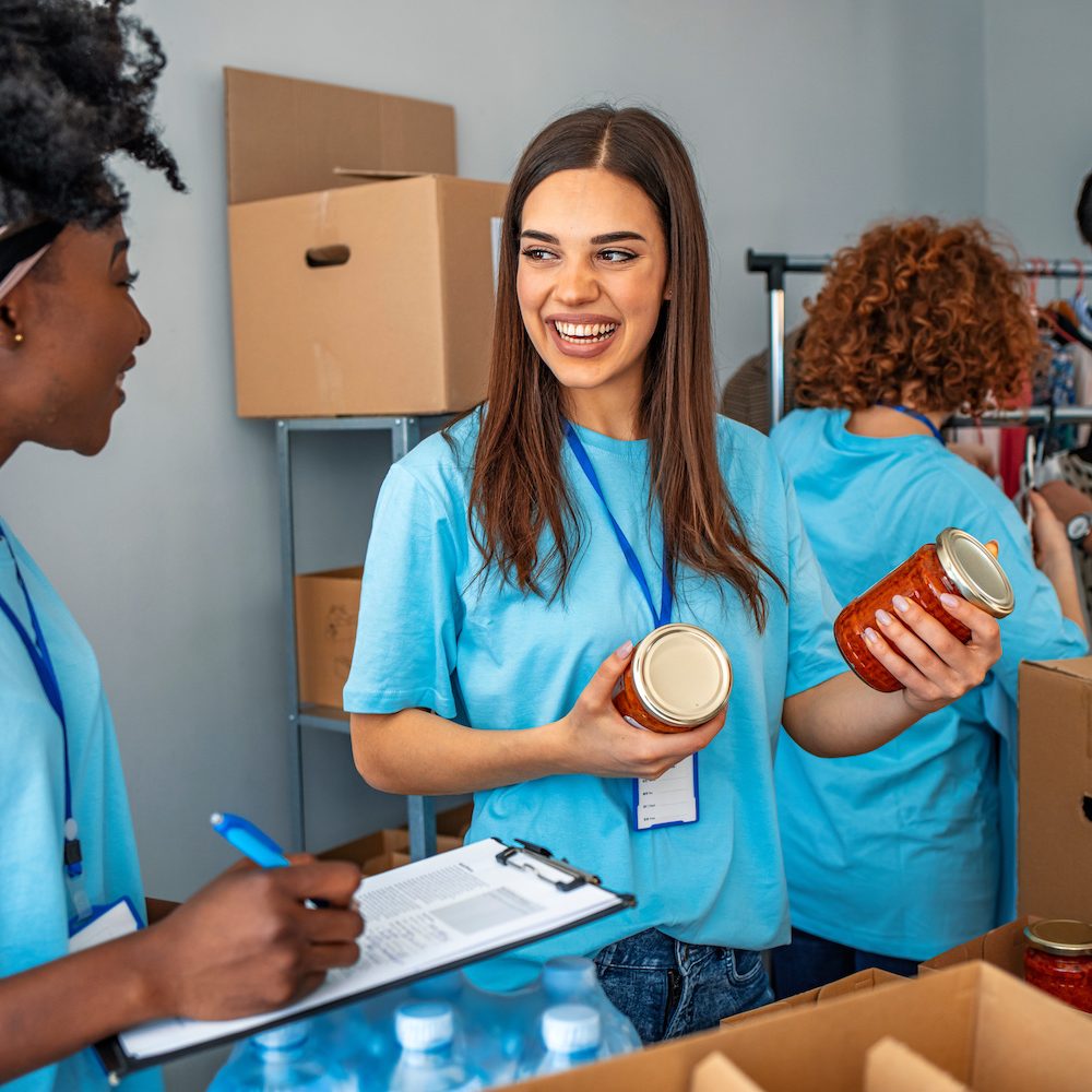 Group of people working in charitable foundation. Happy volunteer looking at donation box on a sunny day. Happy volunteer separating donations stuffs. Volunteers sort donations during food drive
